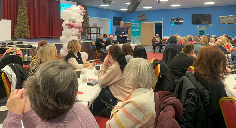 people sitting in groups at table listening to presenter speaking