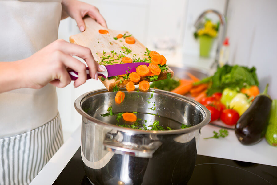 person putting chopped carrots in pot