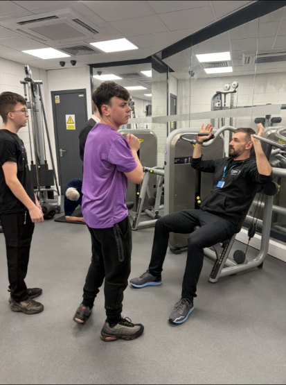Active Schools staff member talks pupils through how to use one of the weight machines in the gym
